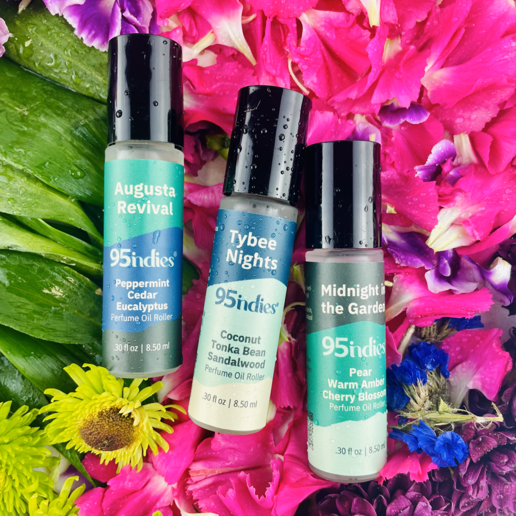 Three 95indies perfume rollers—Augusta Revival, Tybee Nights, and Midnight in the Garden—on vibrant flower petals