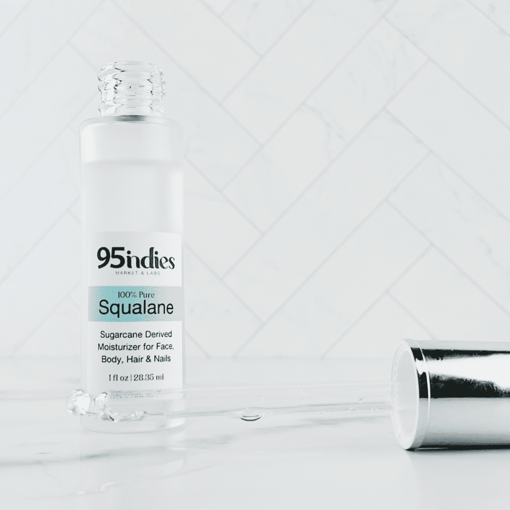 Glass bottle containing squalane which is a hydrating powerhouse with age-well benefits is shown behind a glass dropper containing squalane to display its clarity.