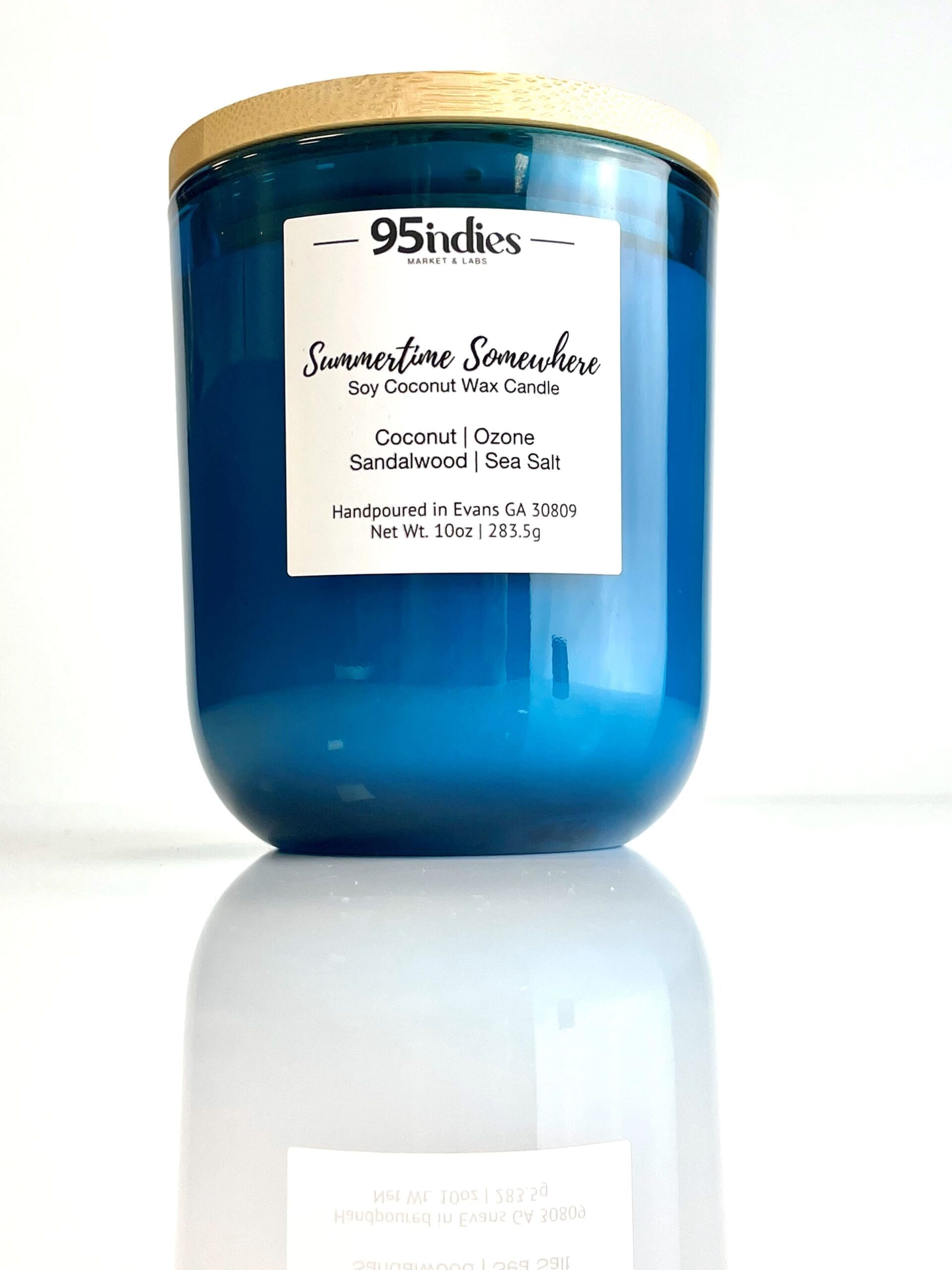 Summertime Somewhere Candle: A luxurious blend of coconut, ozone, sandalwood, and sea salt. Hand-poured in Evans, GA by 95indies Summertime Somewhere soy coconut wax candle in a blue glass jar with a wooden lid, hand-poured by 95indies in Evans, GA.