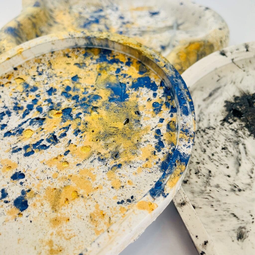 Close-up of handmade Jesmonite trays in bold yellow, blue, and black marbled finishes.
