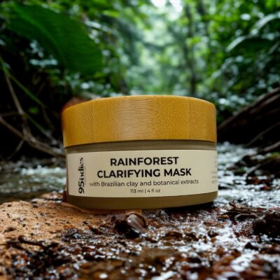 95indies Rainforest Clarifying Mask with bamboo lid, photographed beside a lush stream in a tropical rainforest setting.