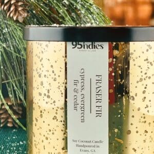 Gold mercury glass candle labeled “Fraser Fir” by 95indies, surrounded by evergreen branches and pinecones.