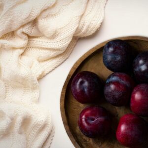 Ripe plum and black cherry with warm amber resin and soft cashmere fabric in natural sunlight