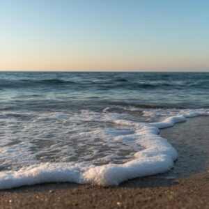 Gentle ocean waves rolling onto sandy shore at sunset with soft golden light and calm sea