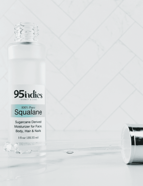 Glass bottle containing squalane which is a hydrating powerhouse with age-well benefits is shown behind a glass dropper containing squalane to display its clarity.